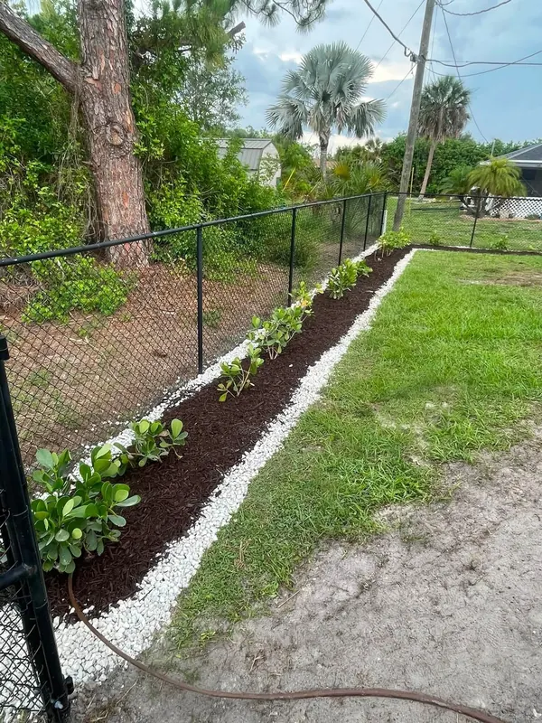 Fence line bed finished with mulch and a white rock border